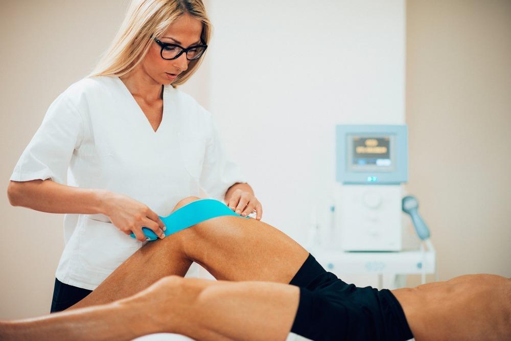 Fysiotherapeut plakt tape op de knie van een patiënt